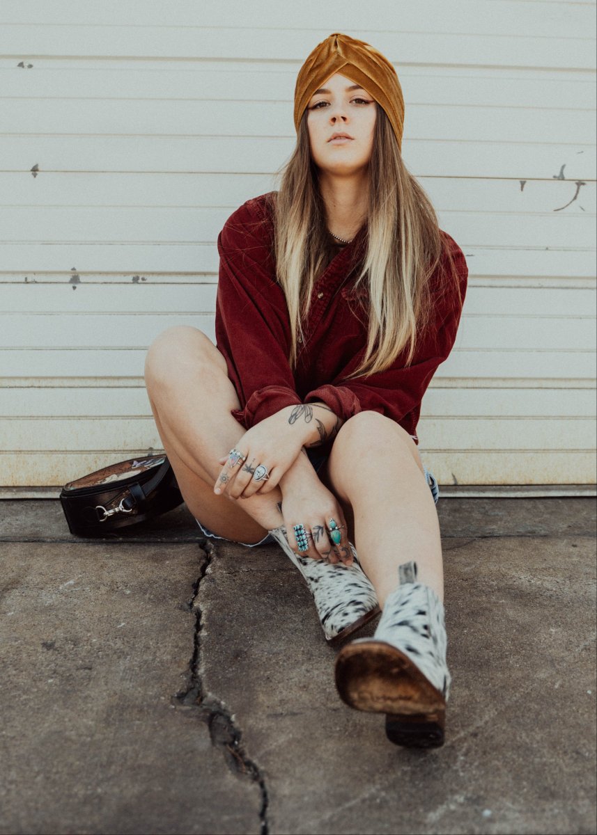 Woman sitting on a concrete step wearing a red jacket, brown turban, and THE AURORA COWHIDE ANKLE BOOTS